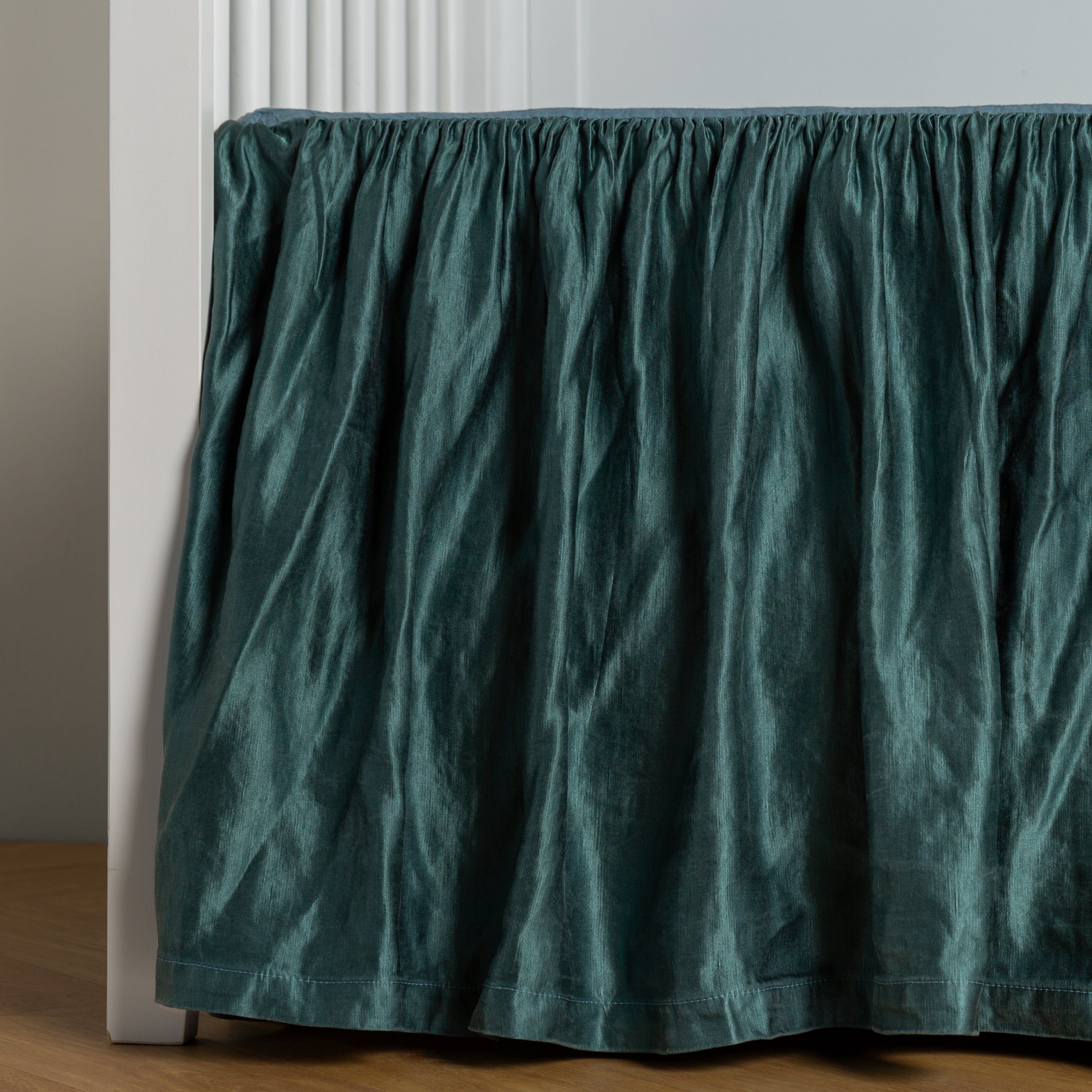 Cenote: charmeuse crib skirt shown on a white crib against a white wall and medium wood floor.