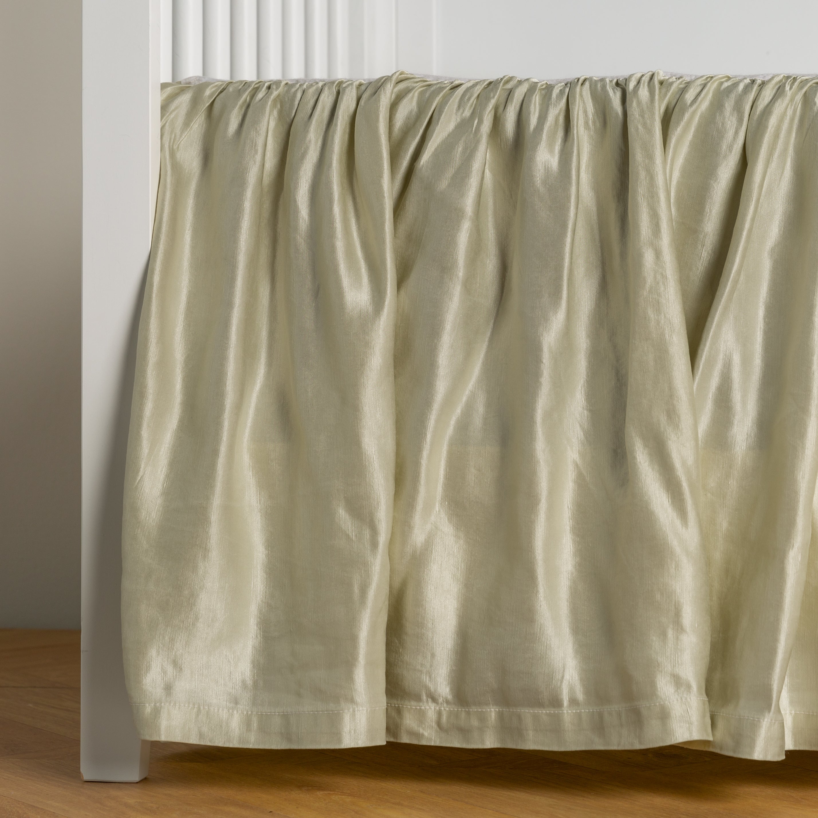 Parchment: charmeuse crib skirt shown on a white crib against a white wall and medium wood floor.
