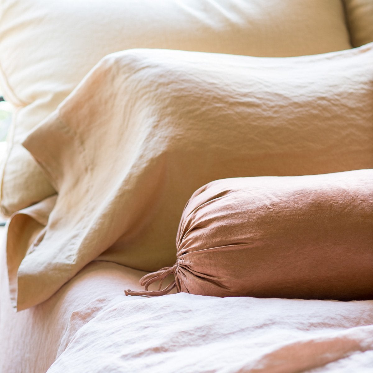 : Paloma sleeping pillow and bolster layered on linen, in pink and gold tones - close-up three-quarter angle.