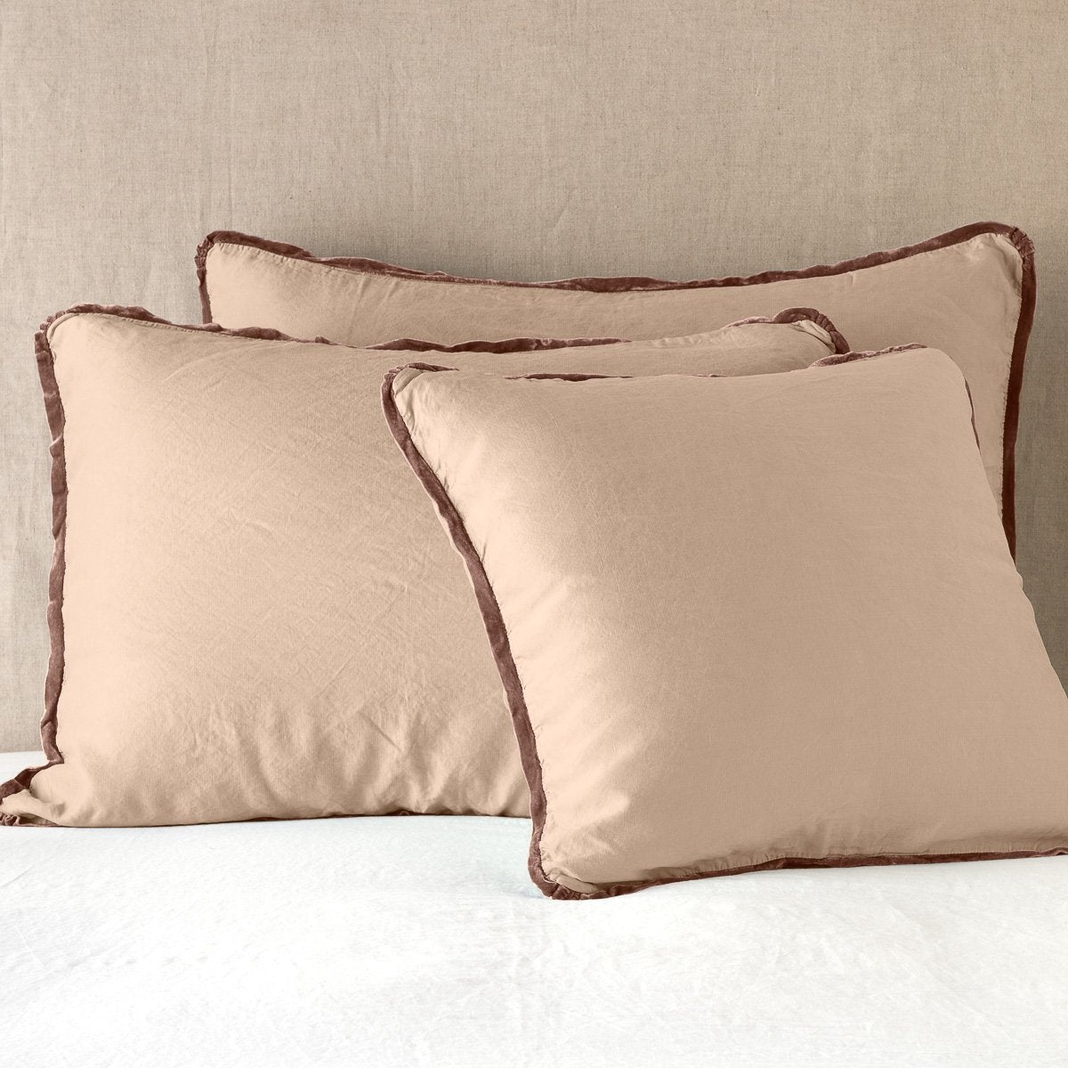 Rouge: shams leaning upright on white sheeting against a neutral headboard.