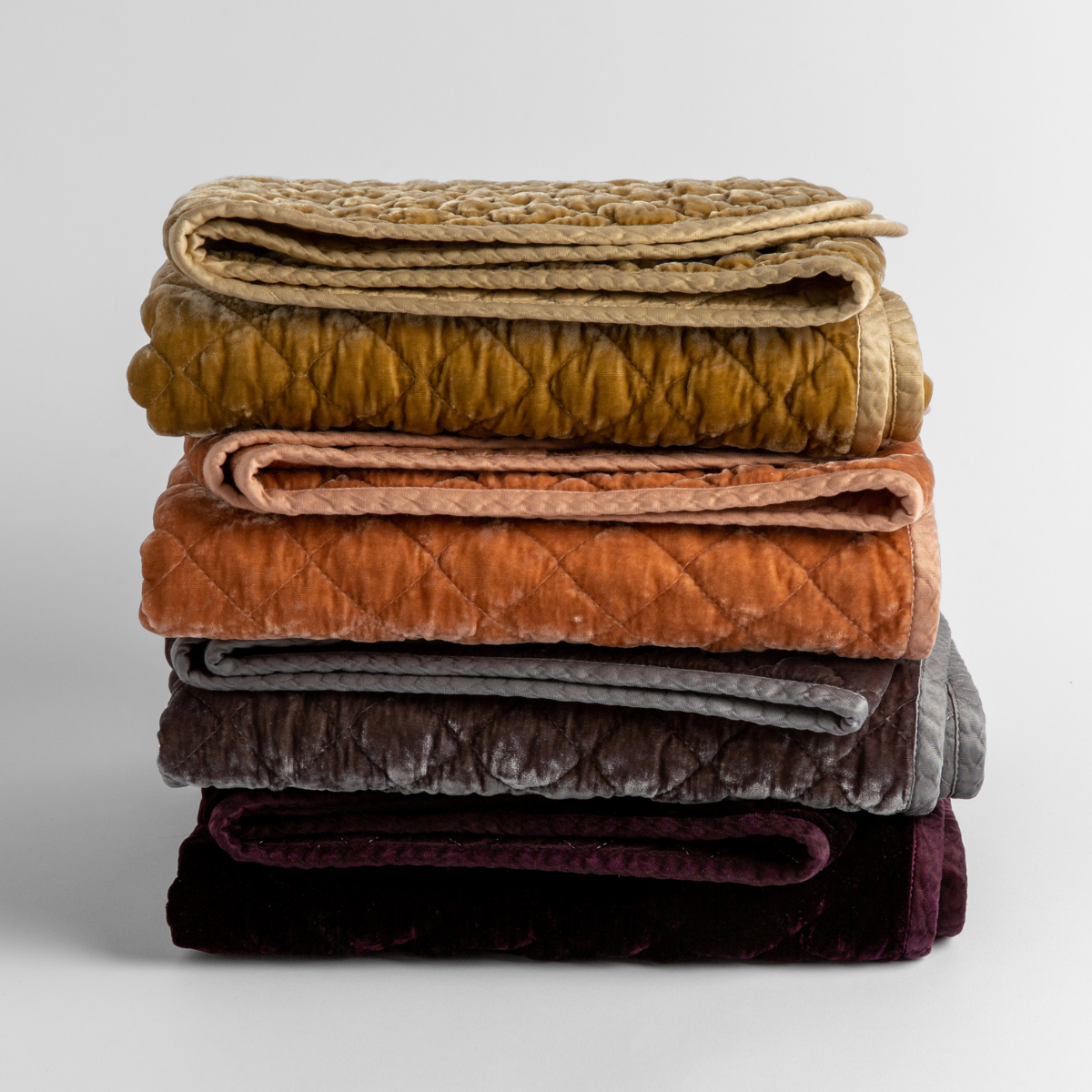 stack of 4 quilted silk velvet baby blankets in honeycomb, rouge, moonlight and fig against a white background.
