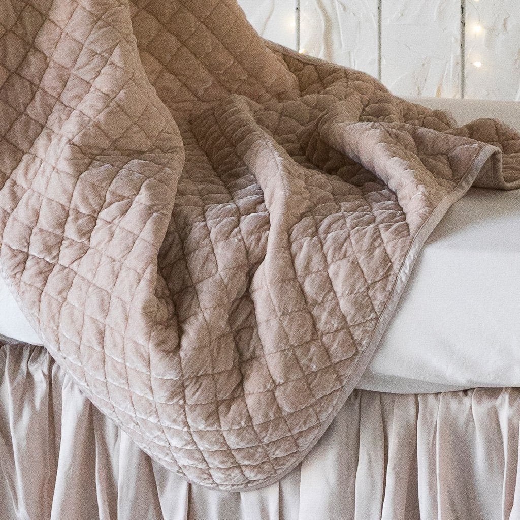Pearl: Close up of silk velvet quilted baby blanket in pearl, draped over a monochromatic crib, showcasing the satin edge trim.