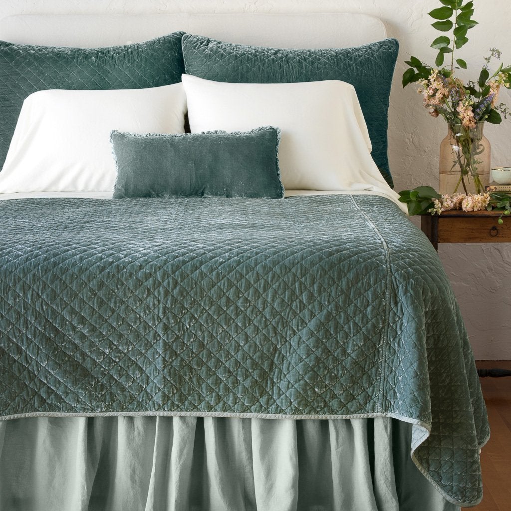 Eucalyptus: shams with matching coverlet on a neatly-made, bed with white sheeting - end of bed view.