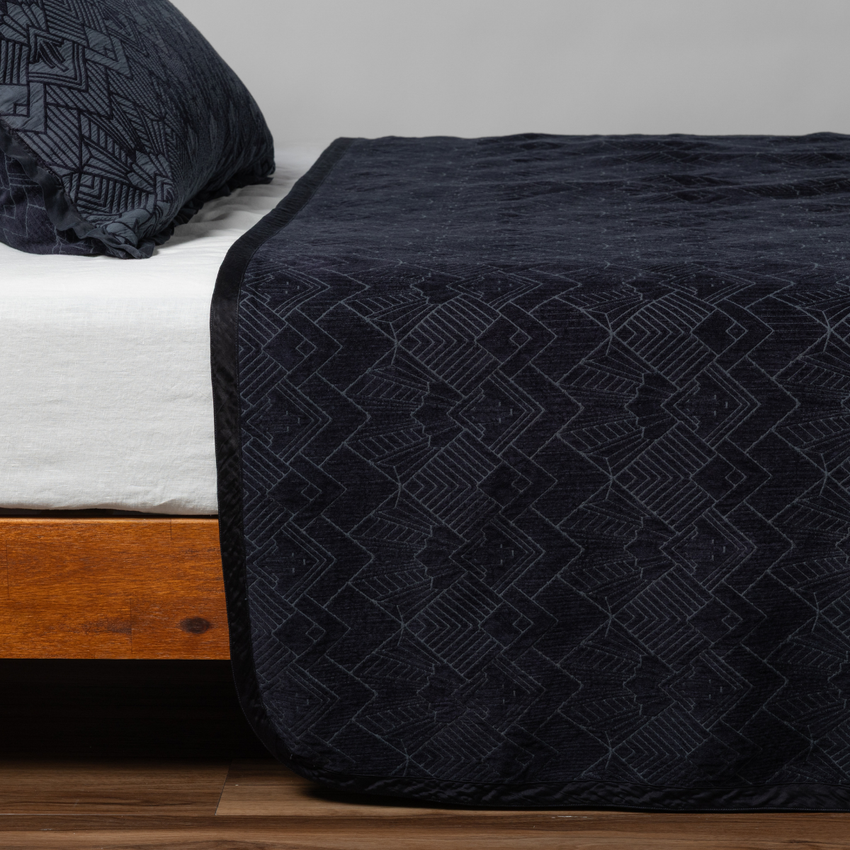 Slate: Matching Trettino Bedspread and Sham in slate, a polished dusky dark blue, shown as the sideview on a bed against a plain background.