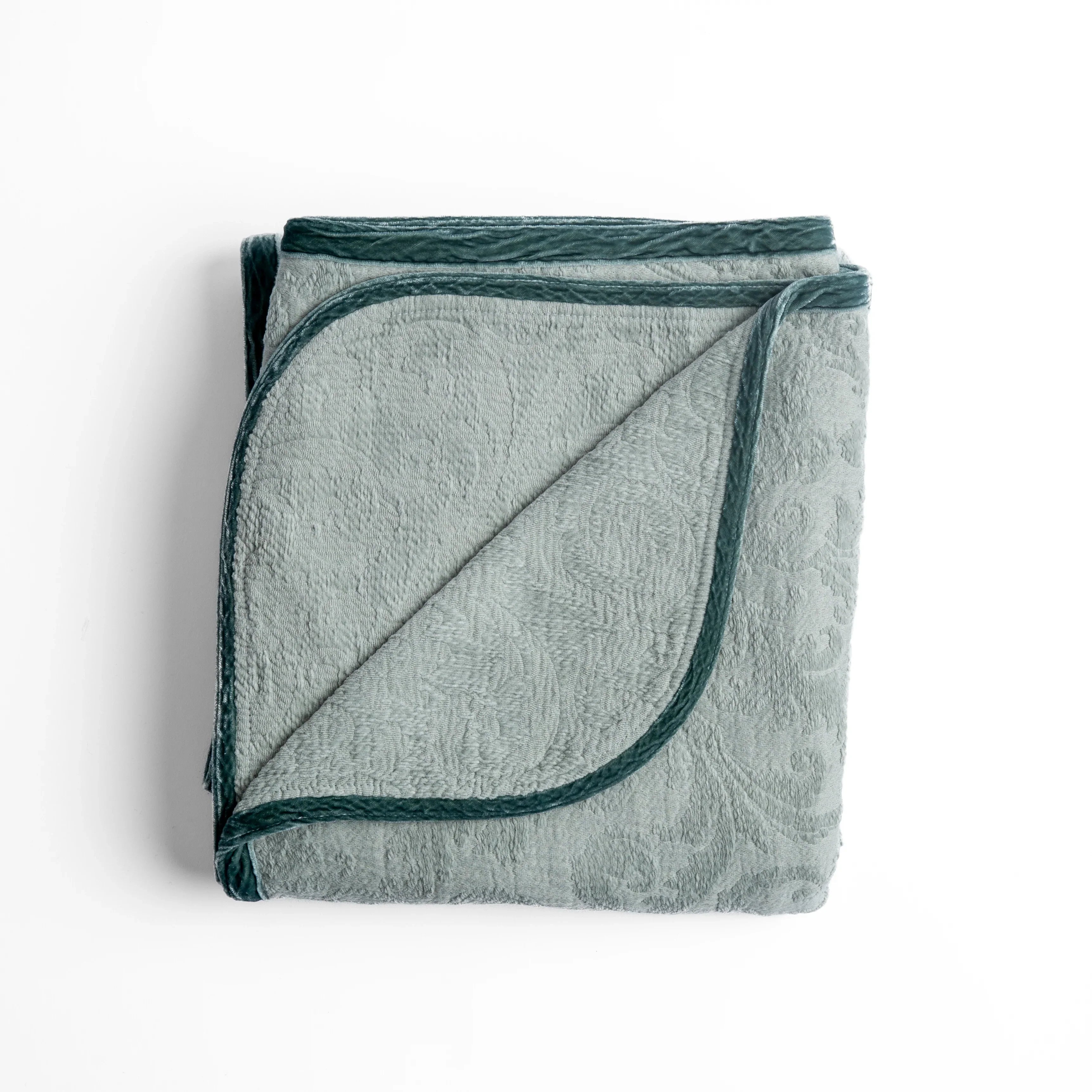 Eucalyptus: folded organic cotton damask throw blanket shown with the corner folded down to show silk velvet trim detail β overhead against a plain white background.