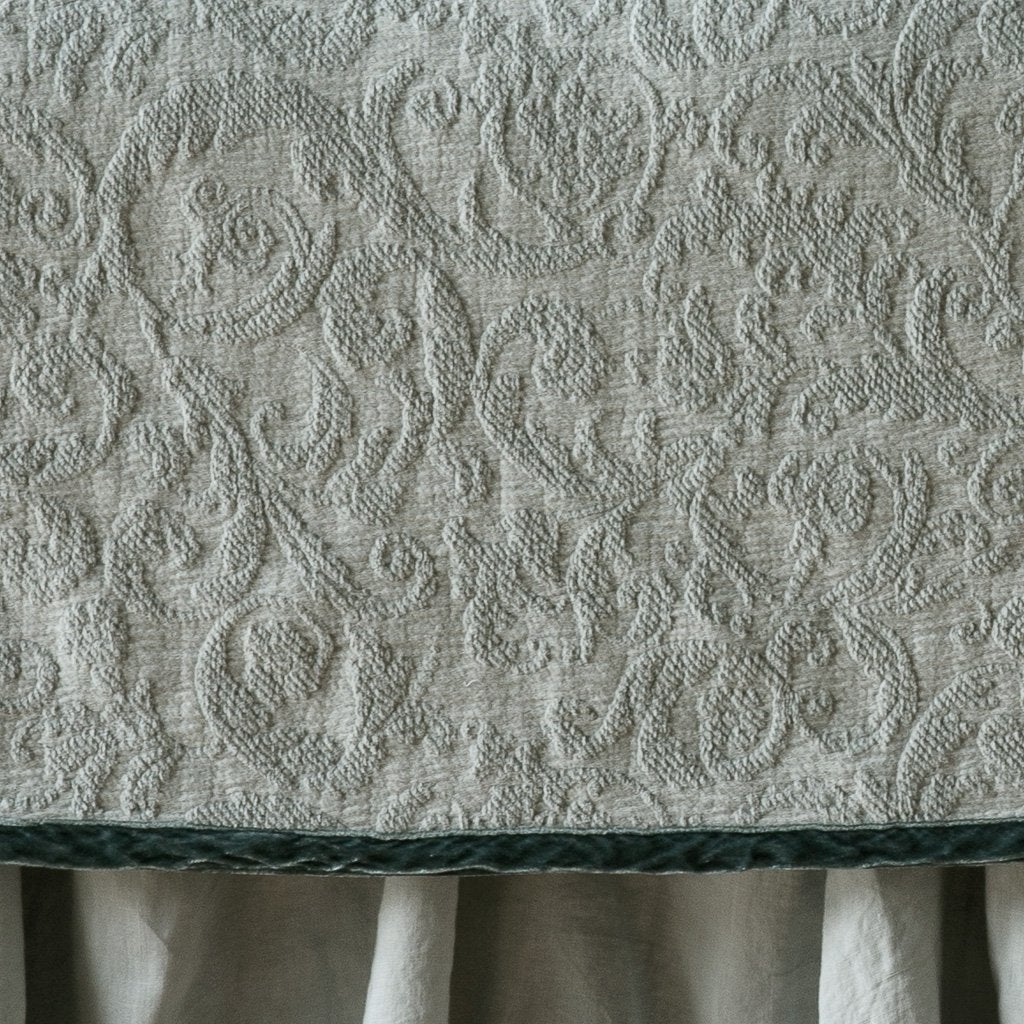 Eucalyptus: Close up of the Adele coverlet in eucalyptus, highlighting the detail of the cotton damask and the silk velvet edging trim. A white bed skirt peeks out at the bottom of the shot.
