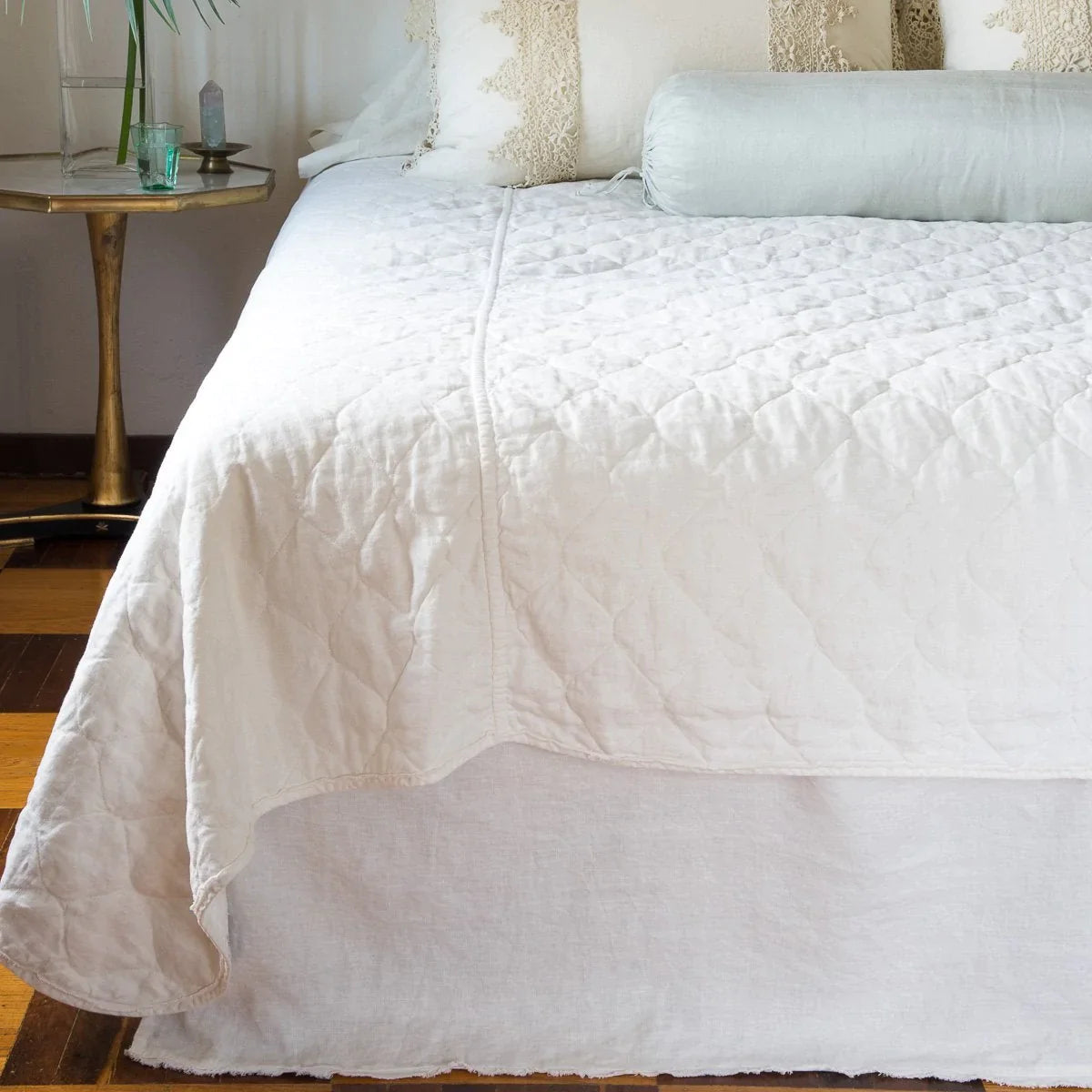 : Austin bed skirt in winter white, shown from the end of the bed, layered with a quilted coverlet in the same tone.