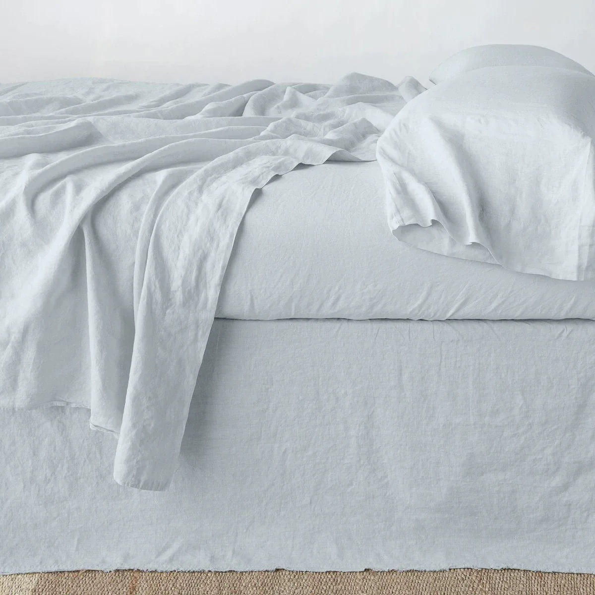 Cloud: Austin bed skirt in cloud shown from the side on a bed with monochromatic sheeting, highlighting its tailored, ungathered style.