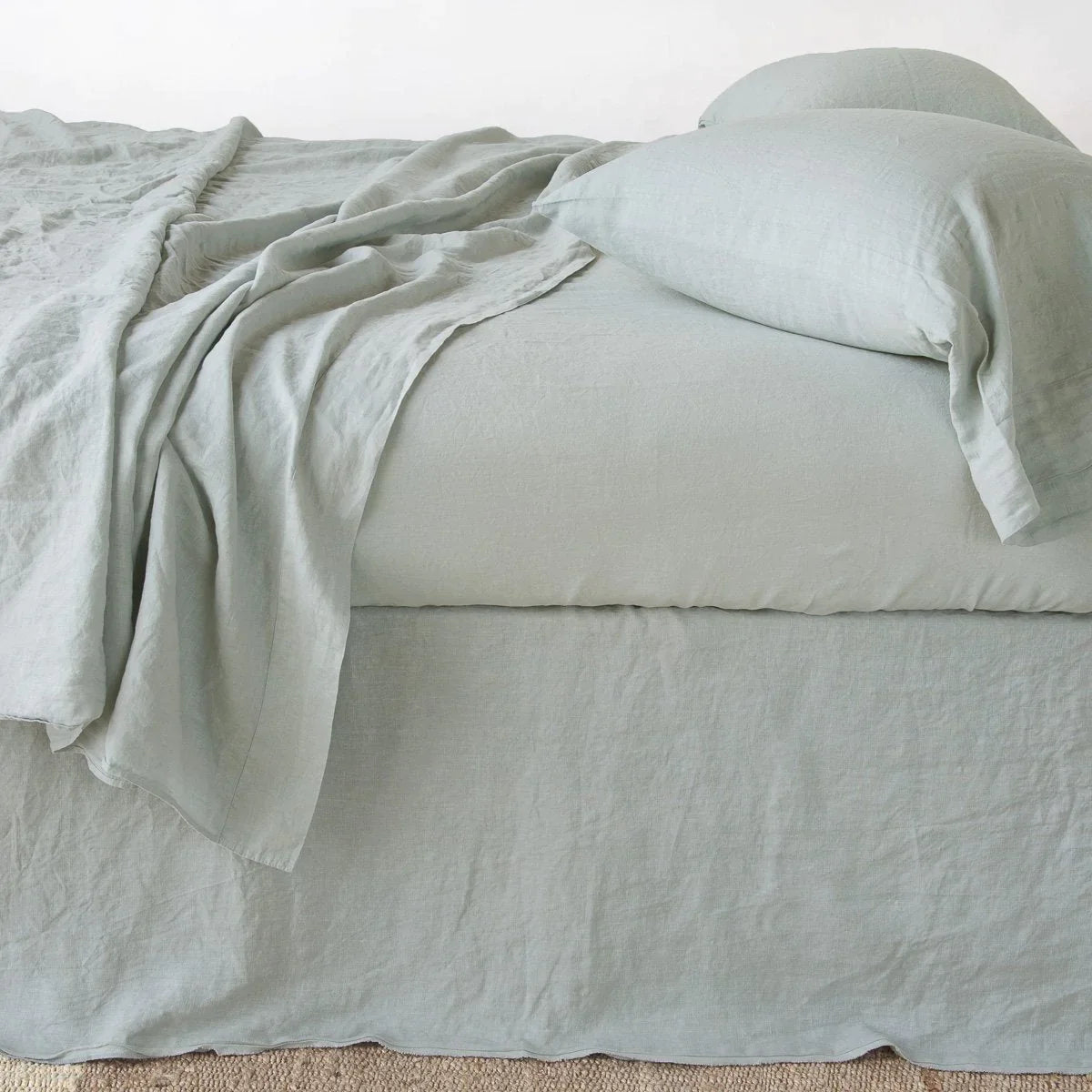 Eucalyptus: Austin bed skirt in eucalyptus shown from the side on a bed with monochromatic sheeting, highlighting its tailored, ungathered style.