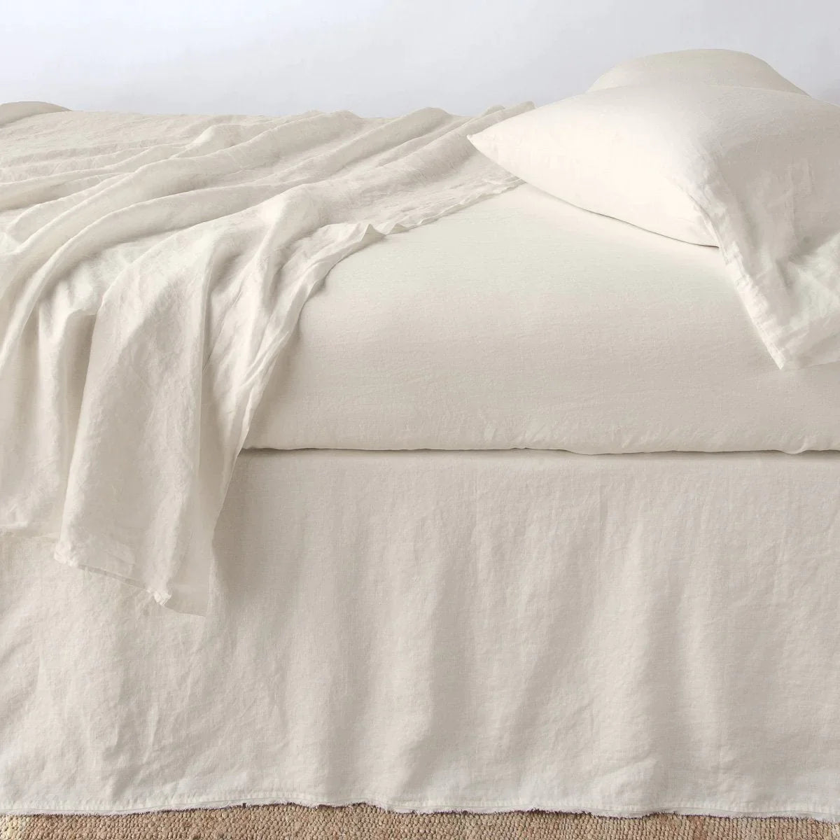 Parchment: Austin bed skirt in parchment shown from the side on a bed with monochromatic sheeting, highlighting its tailored, ungathered style.