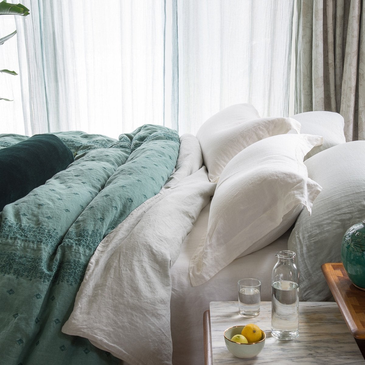 : Linen shams in white and matching sheeting, mixed with other textures of embroidered linen and silk velvet in jade - side view.