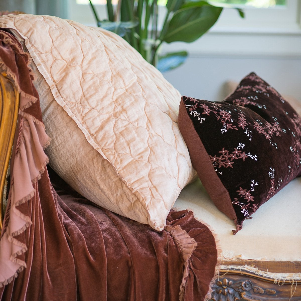 : Luna coverlet on a fig bed, with mixed textures of cotton velvet, embroidered linen, tassled silk charmeuse, and silk velvet. Deep blue throw pillows and dark blue background create a moody vibe.
