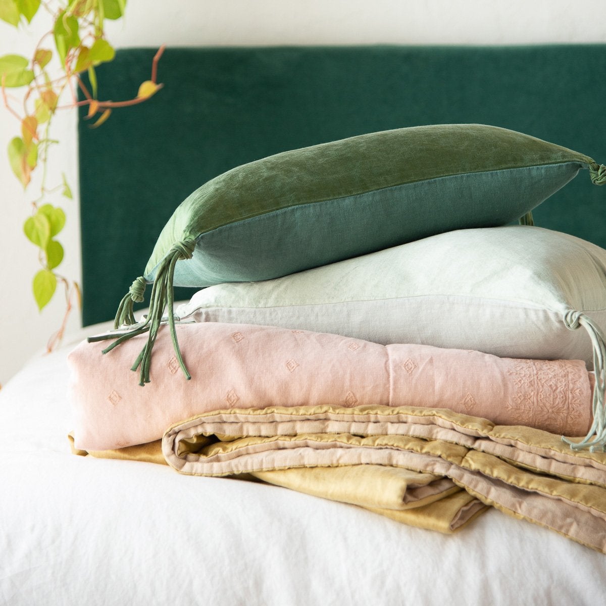 : Ines throw blanket in rouge, folded and stacked with white, gold, and green tones - side view.