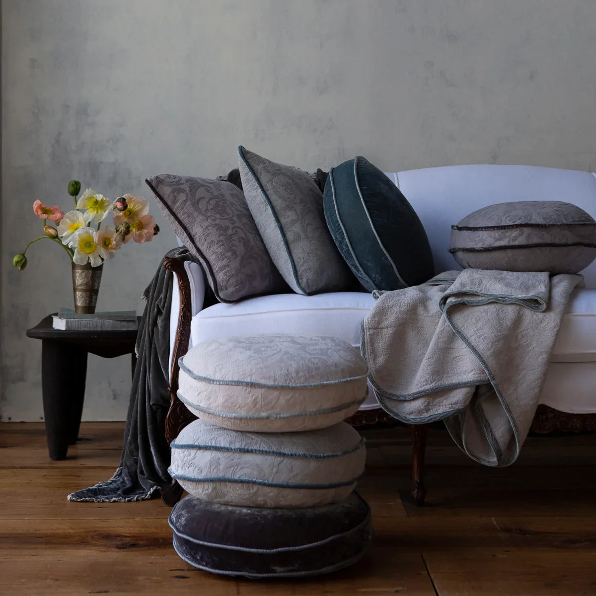 : Adele throw pillows and blanket on white couch. Shown in several cool tones with flowers on side table.