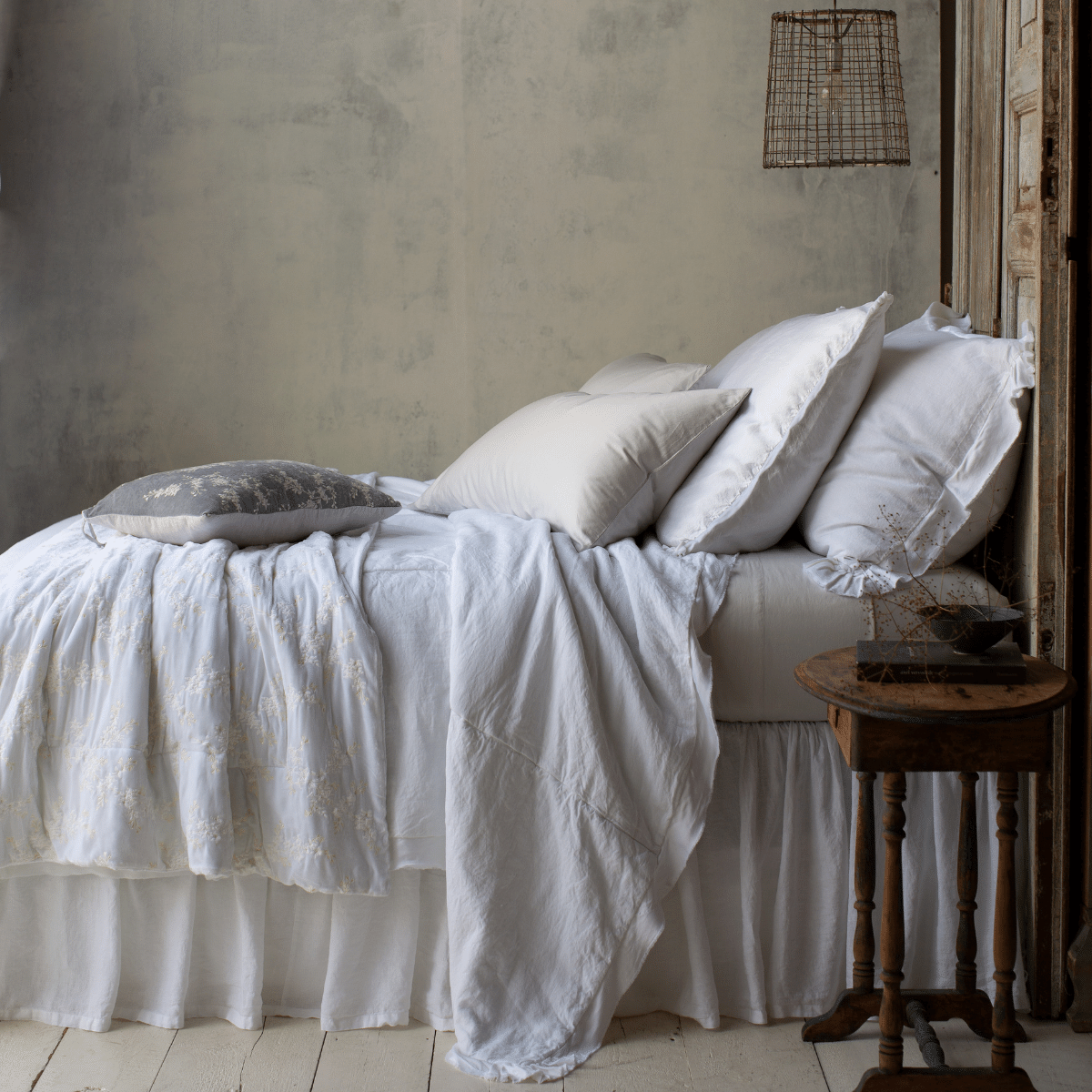 : embroidered silk velvet 15x24 pillow in sterling on a mostly all-white bed. Bed shown from the side with a neutral background and floor.