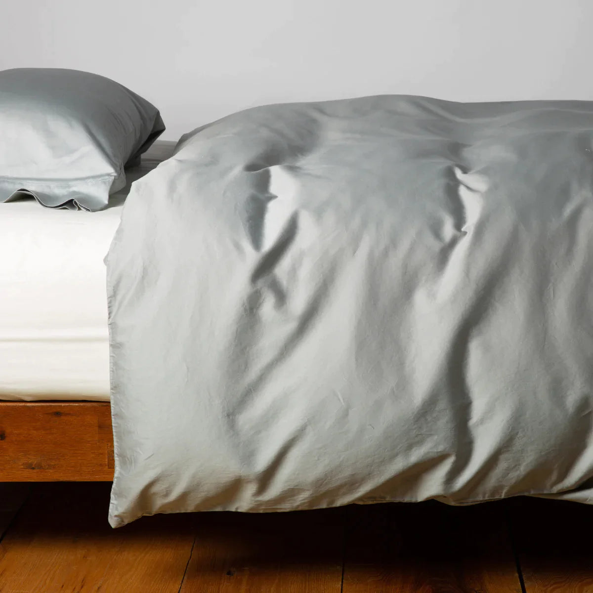 : Cotton sateen duvet cover in mineral with matching sleeping pillow on white sheeting - side view.
