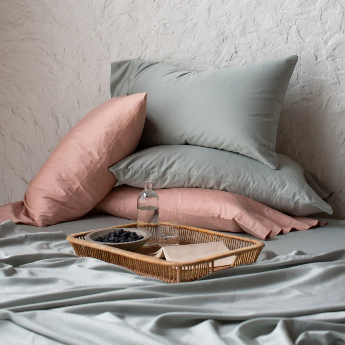 : Bria flat sheet in white, shown folded over a coverlet from an overhead angle, with side by side sleeping pillows in white and midnight blue.