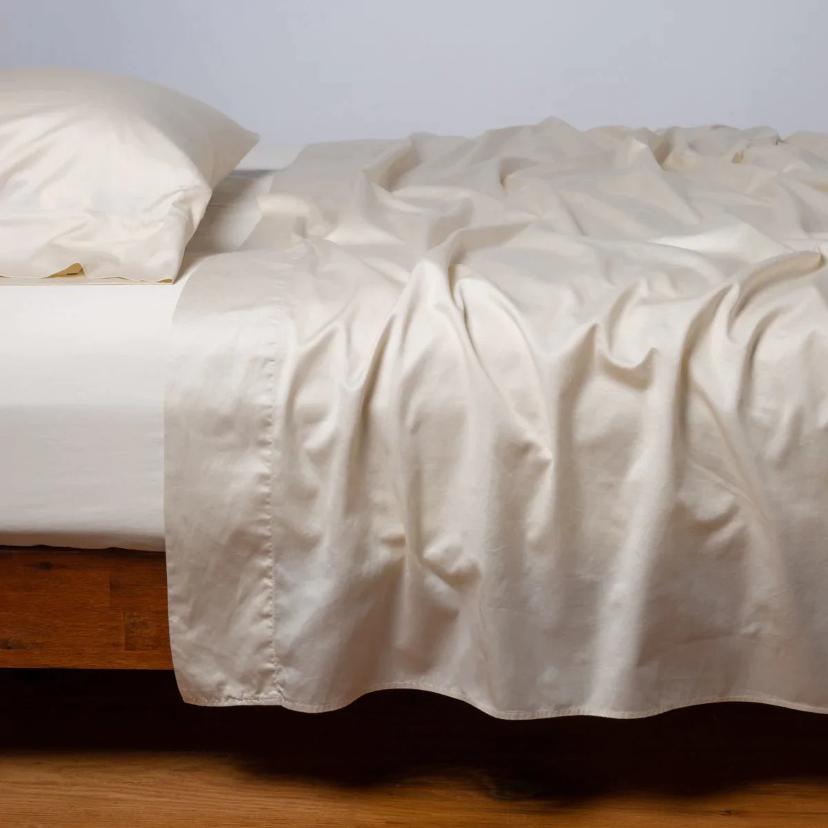 : Bria flat sheet in parchment, shown with matching fitted sheet and sleeping pillow - side view.