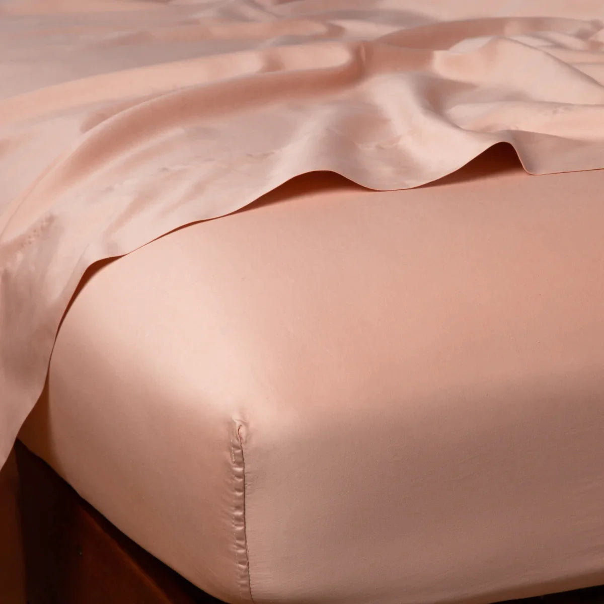 Rouge: Cotton sateen flat sheet draped over matching fitted sheet. Shown from the top corner, the flat sheet is rumpled, highlighting the shine of the fabric.