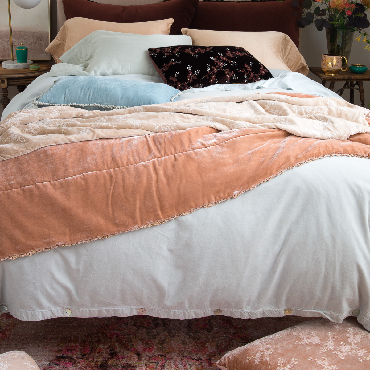 : Carmen throw blanket in rouge layered under silk velvet throw pillows and blankets in light neutrals, soft blues, and deep browns - end of bed view.