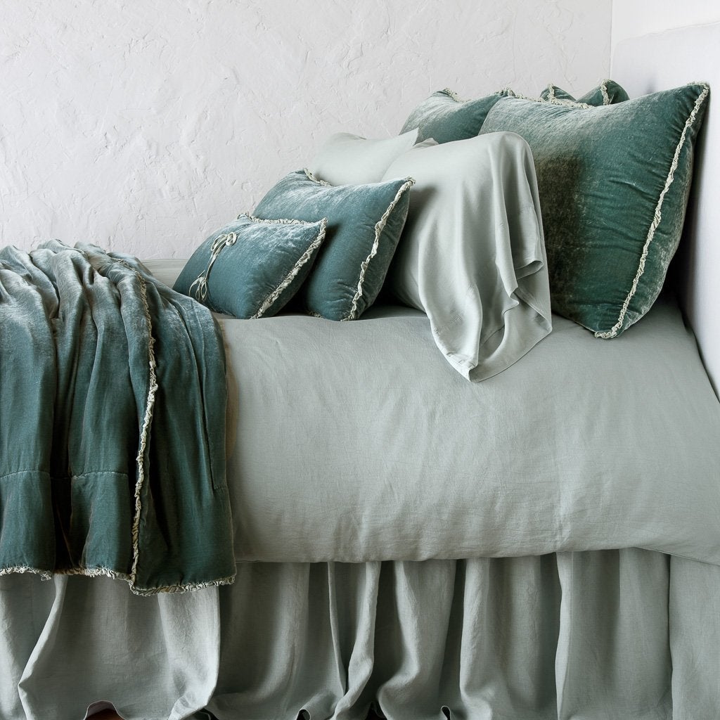 Eucalyptus: Silk velvet lumbar pillow with petite ruffle on a monochromatic, neatly made bed with matching accessory pieces - side view.