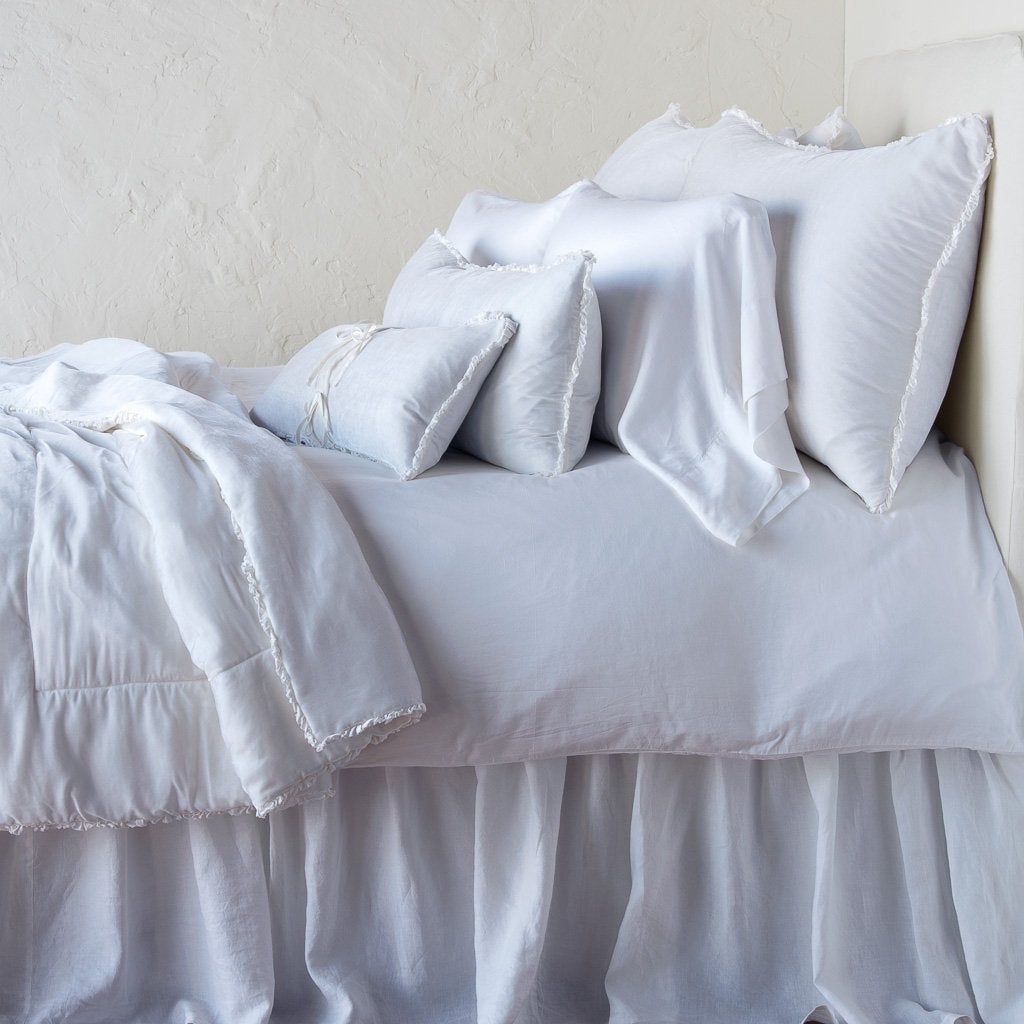 White: Silk velvet lumbar pillow with petite ruffle on an all white, neatly made bed with matching accessory pieces - side view.