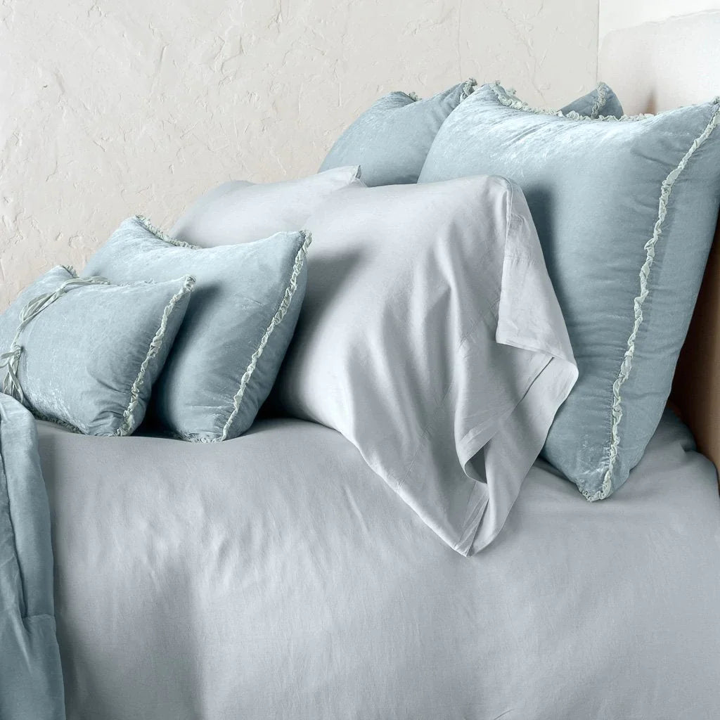 Cloud: Silk velvet shams with a petite ruffle on monochromatic bed, leaning upright behind sleeping and throw pillows - side view.