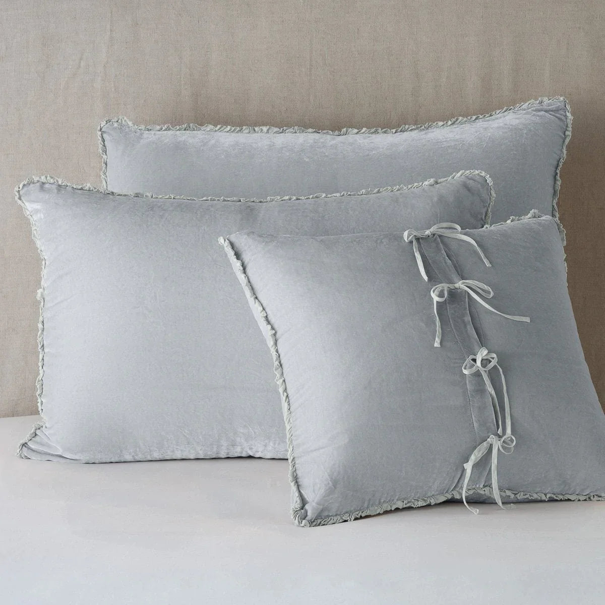Sterling: Silk velvet shams with a petite ruffle leaning upright against a neutral headboard. The front sham is backwards, showcasing the charmeuse tie closures.