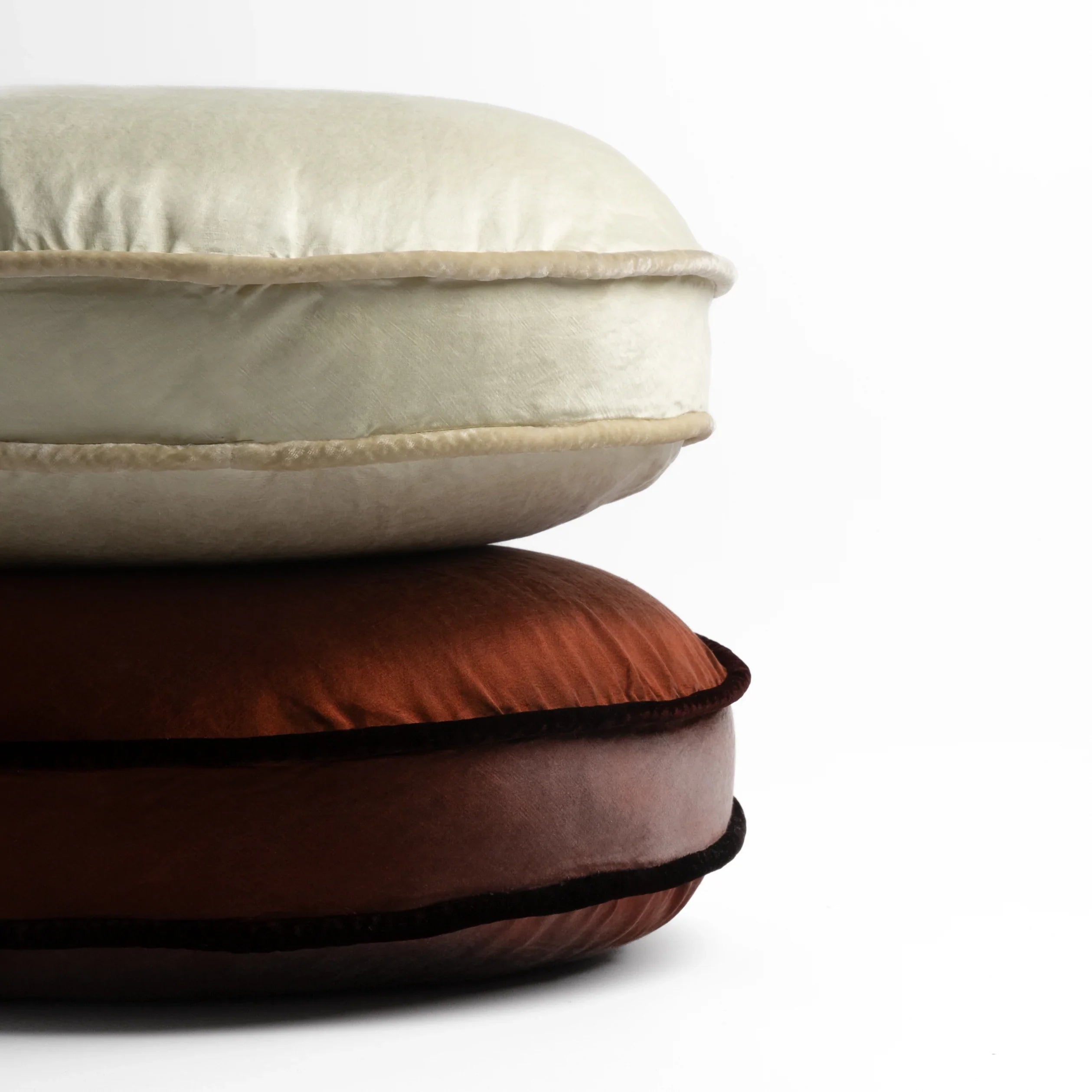 : two 18-inch round pillows stacked against a white background, showing the silk velvet trim on the pillow gussets — Parchment and Mahogany
