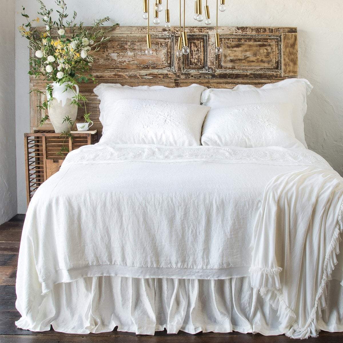 : Delphine coverlet in white on an all-white beed with shams, sleeping pillows, throw blanket and bed skirt - end of bed view.