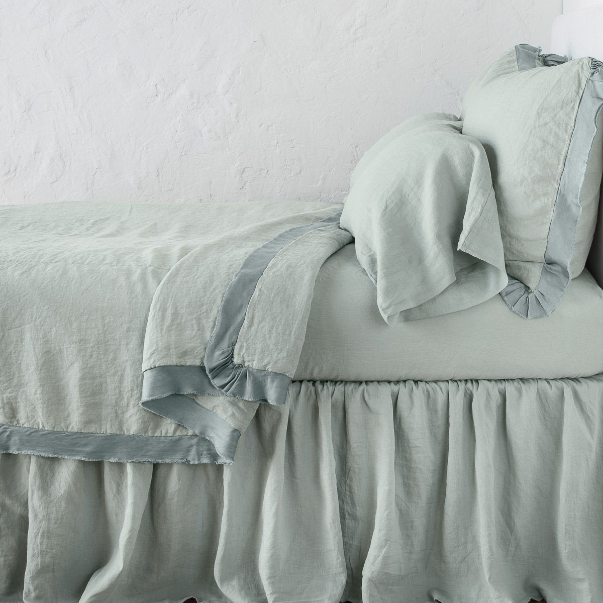 Eucalyptus: satin trimmed linen coverlet on monochromatic bed with corner pulled back to reveal sheet, bed skirt - side view.