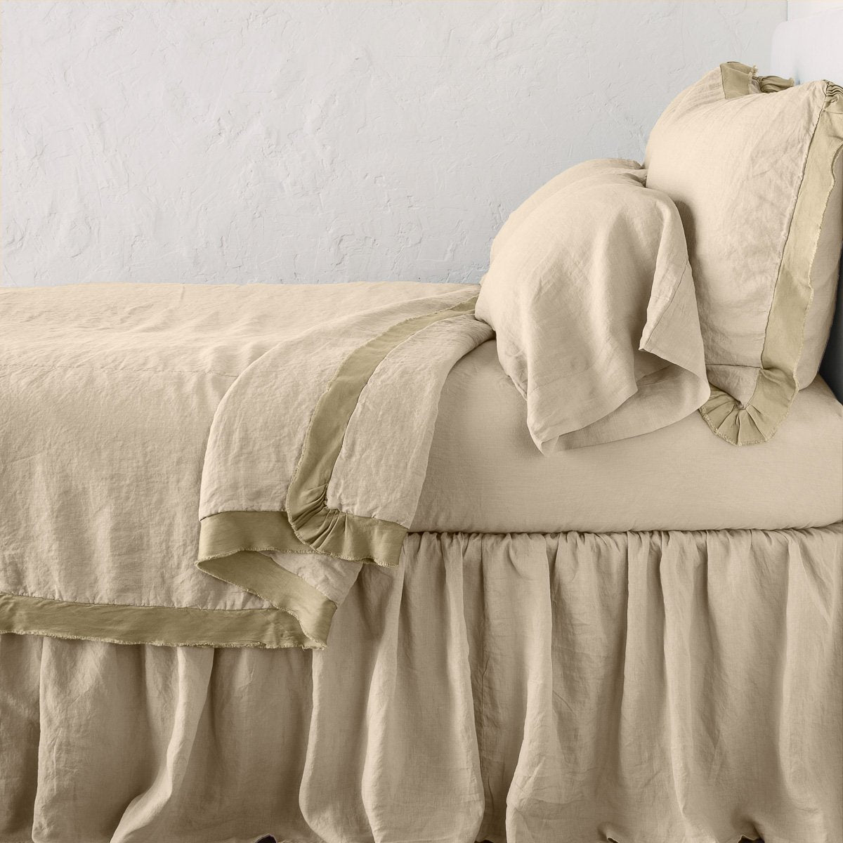 Honeycomb: satin trimmed linen coverlet on monochromatic bed with corner pulled back to reveal sheet, bed skirt - side view.