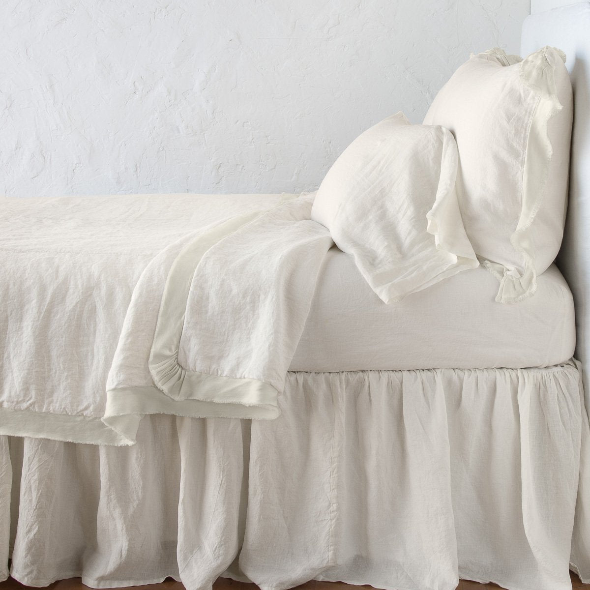 Parchment: satin trimmed linen coverlet on monochromatic bed with corner pulled back to reveal sheet, bed skirt - side view.