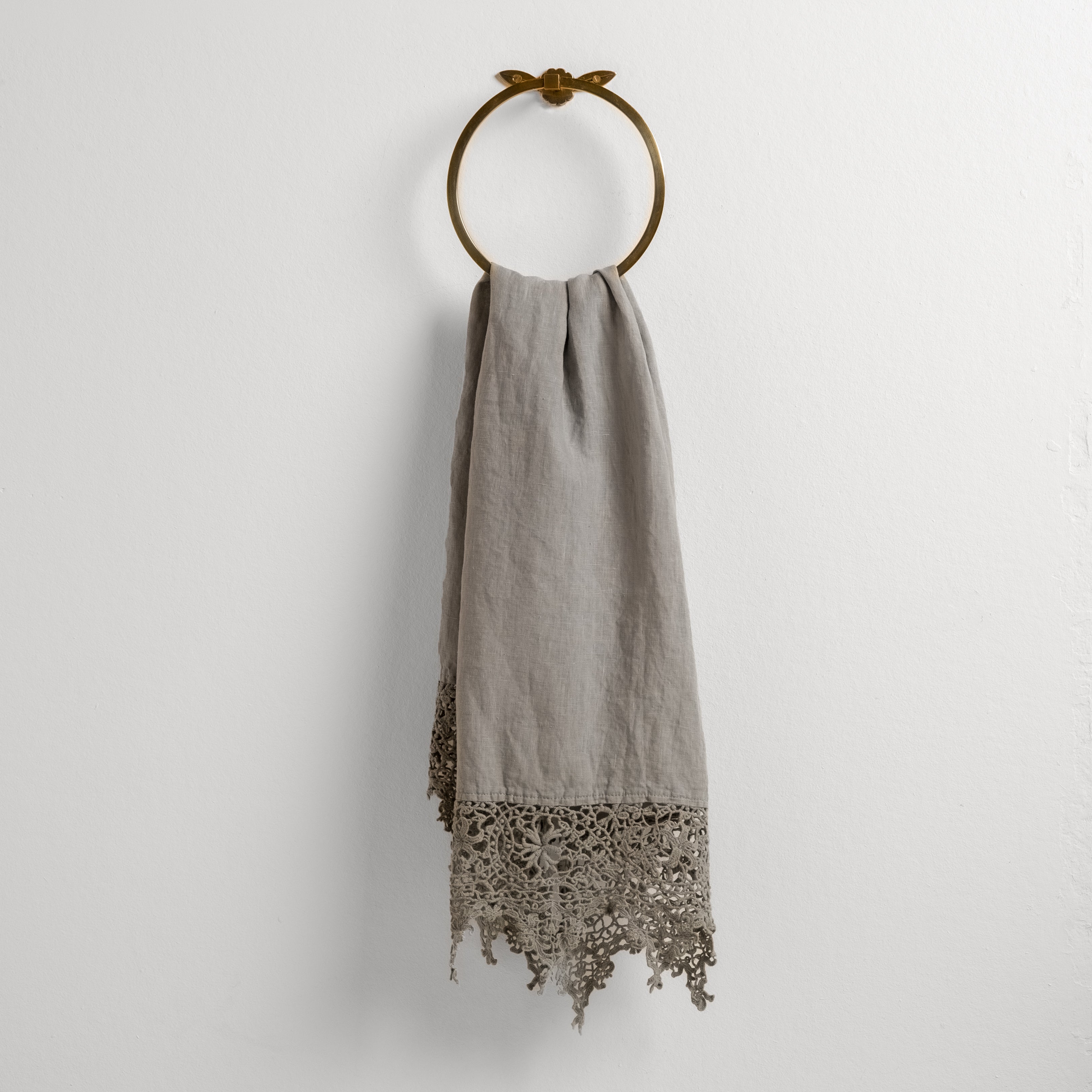 Mineral: Lace trimmed linen guest towel draped through a decorative towel ring against a plain white background.