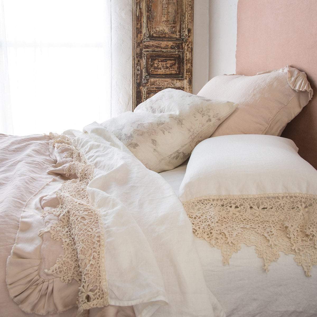 : Frida flat sheet in winter white, folded back over soft pink bedding, highlighting the antique cotton lace trim - close up side view.