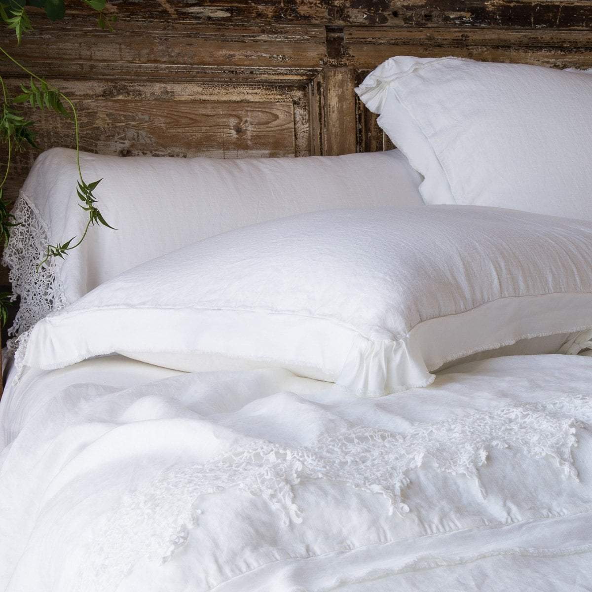 : Frida flat sheet and pillowcase on an all white, primarily linen bed. Cropped view from end of bed with distressed wood headboard.