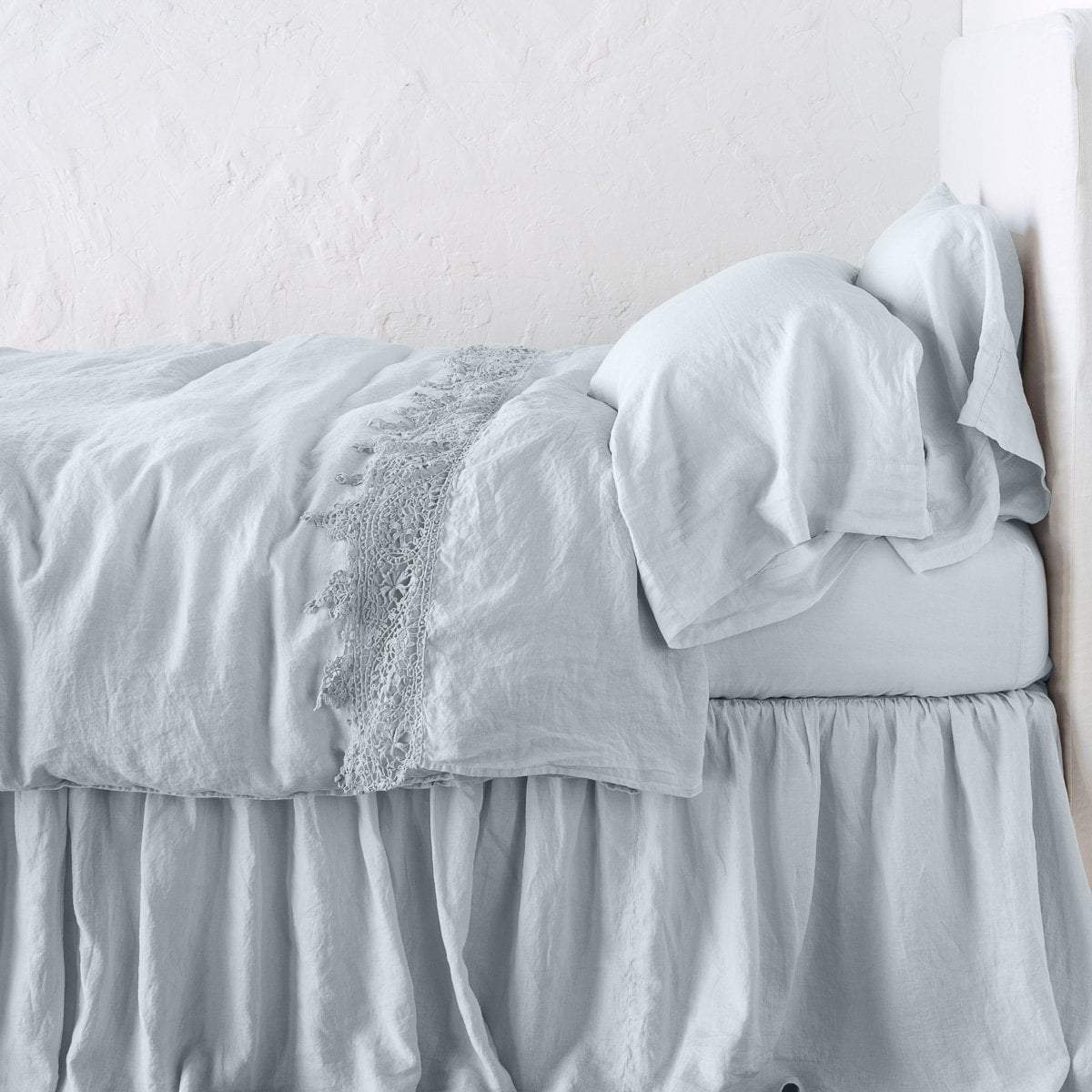 : Frida flat sheet in cloud, folded back over monochromatic linen bed- side view.