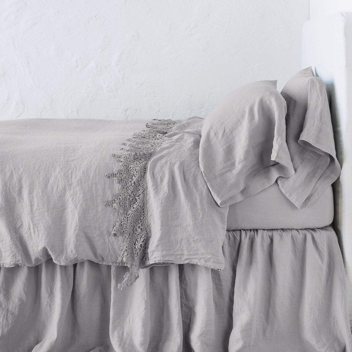 Fog: Lace trimmed linen flat sheet folded back over monochromatic linen bed - side view.