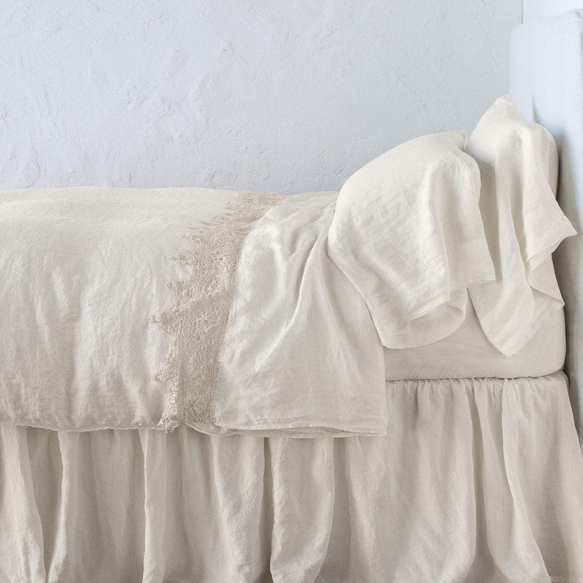 Parchment: Lace trimmed linen flat sheet folded back over monochromatic linen bed - side view.