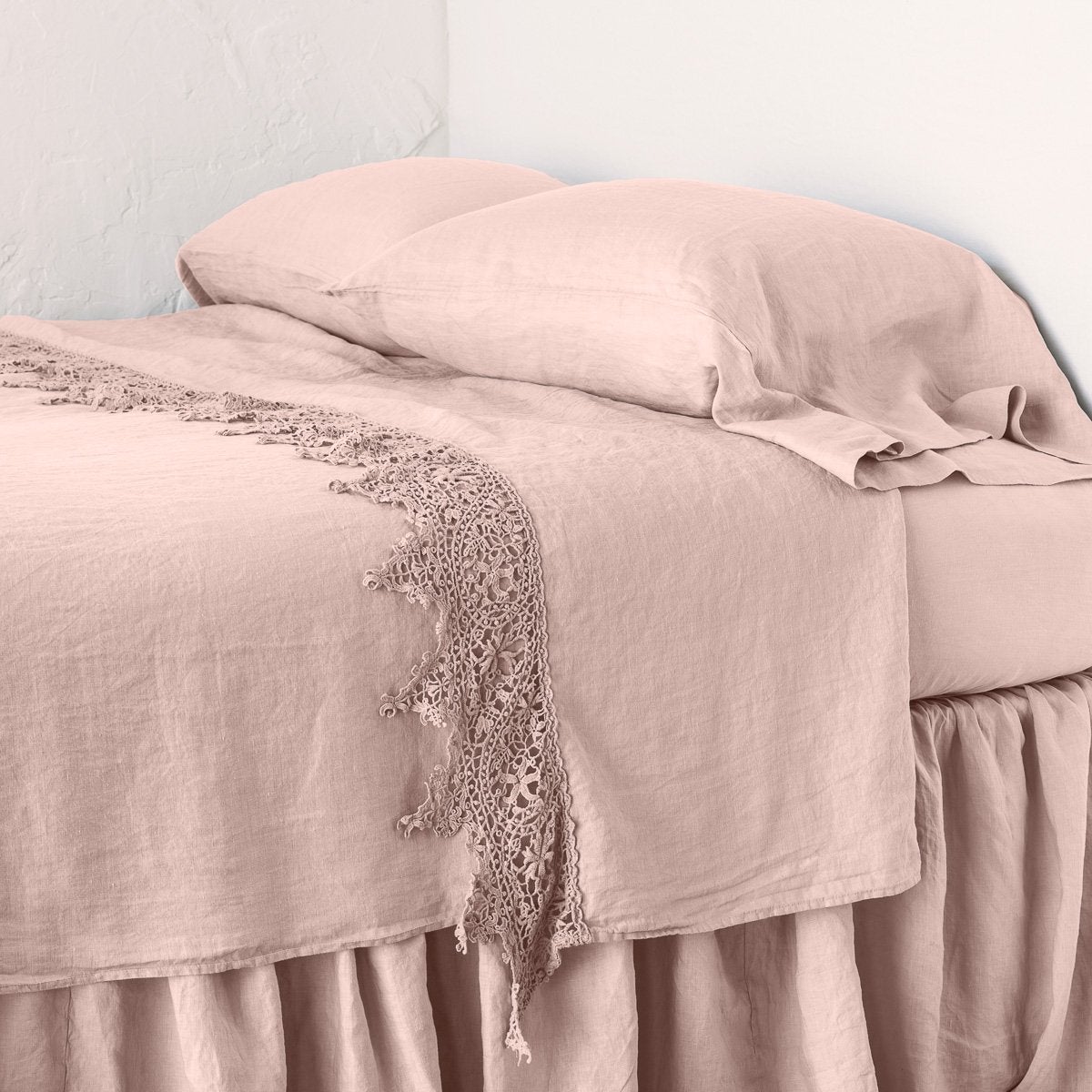 Rouge: Lace trimmed linen flat sheet neattly folded back on a monochromatic linen bed - cropped three-quarter angle.