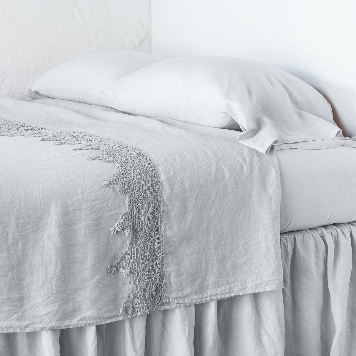 Sterling: Lace trimmed linen flat sheet neattly folded back on a monochromatic linen bed - cropped three-quarter angle.