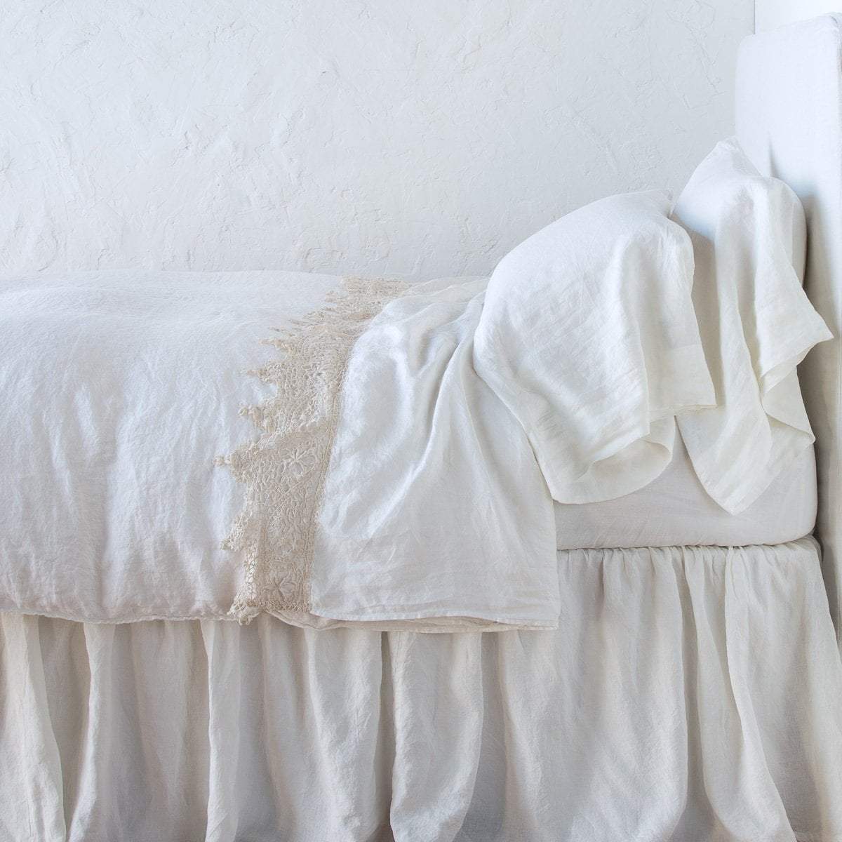 Winter White: Lace trimmed linen flat sheet folded back over monochromatic linen bed - side view.