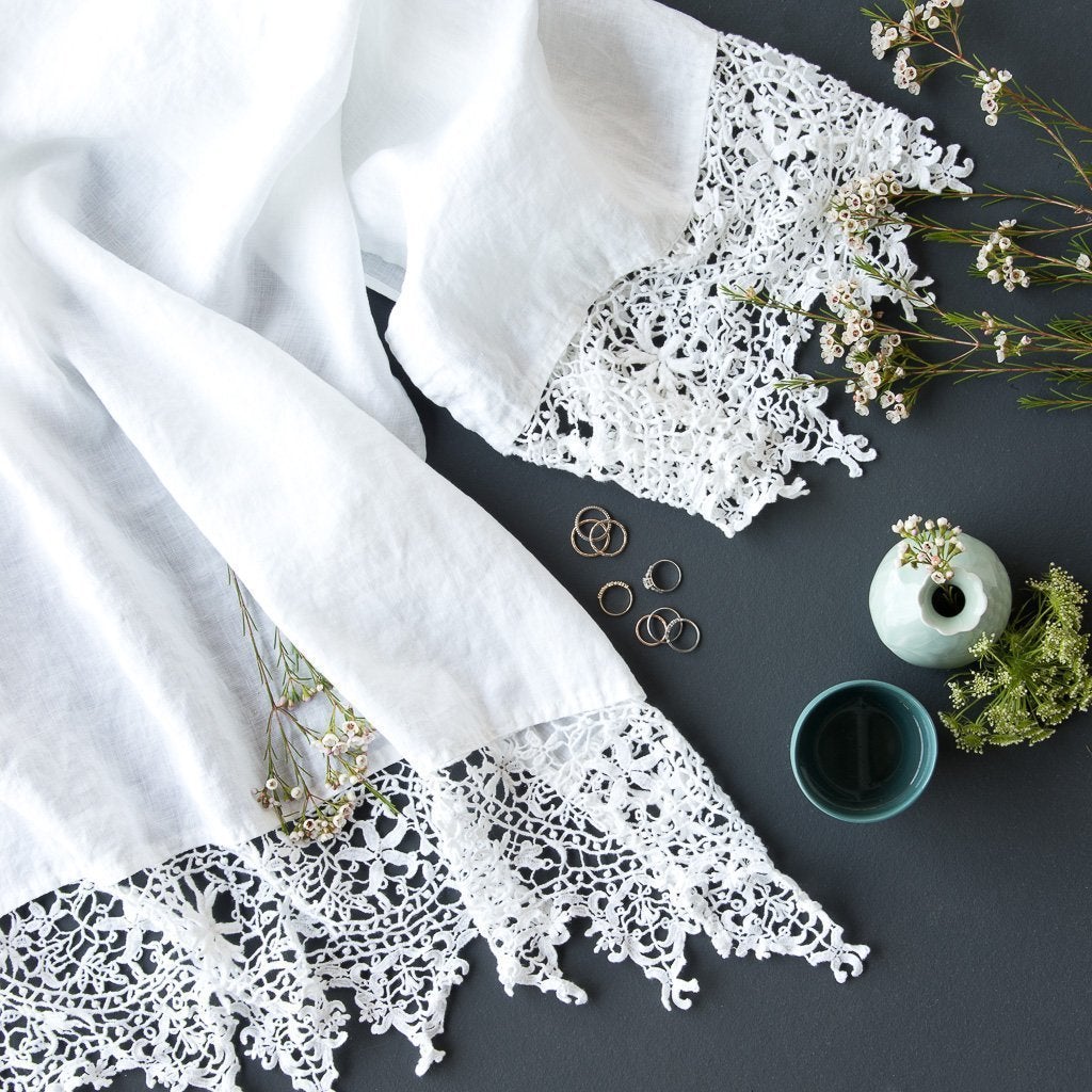: Frida guest towel in white draped on a dark background with blue green vases and delicate flowers - overhead view.