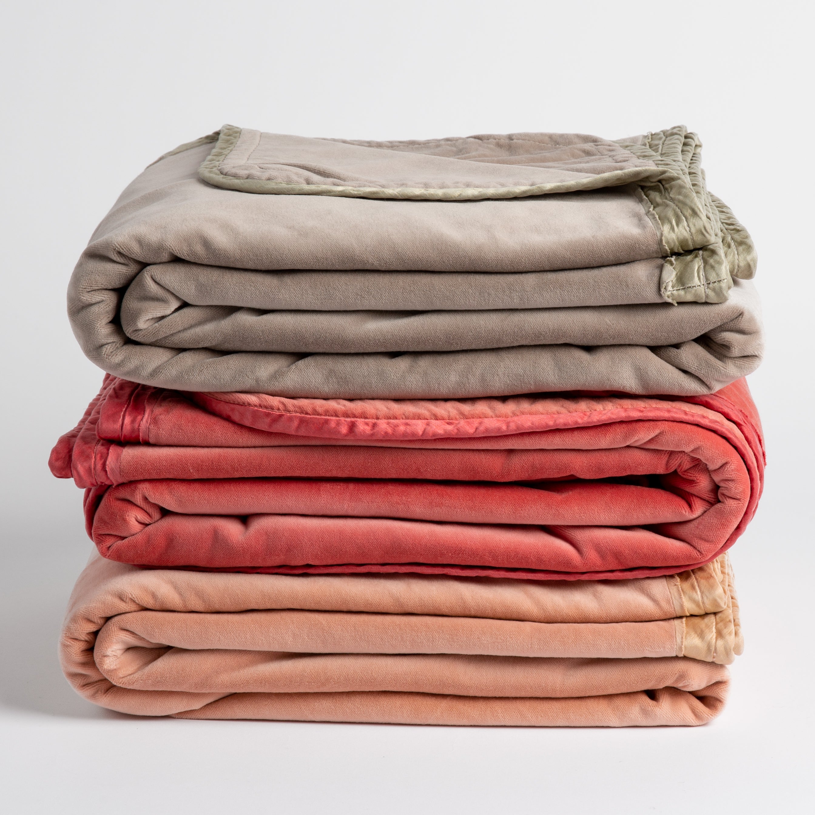 : three cotton velvet throw blankets in fog, poppy and rouge stacked with charmeuse trim visible. Shot straight on against a plain white background.