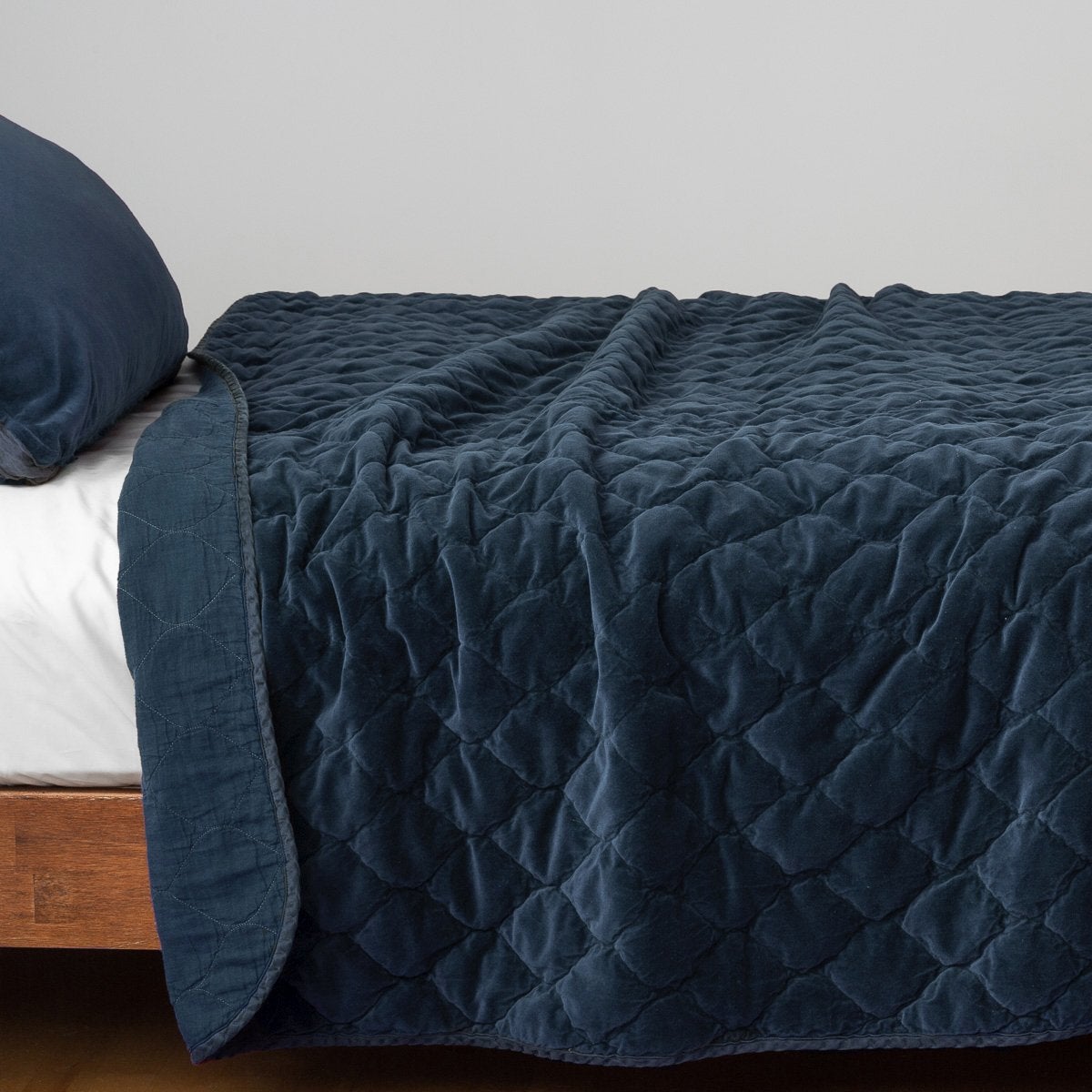 Midnight: Quilted cotton velvet coverlet, with top folded back to showcase linen back, draped over a white fitted sheet - side view.