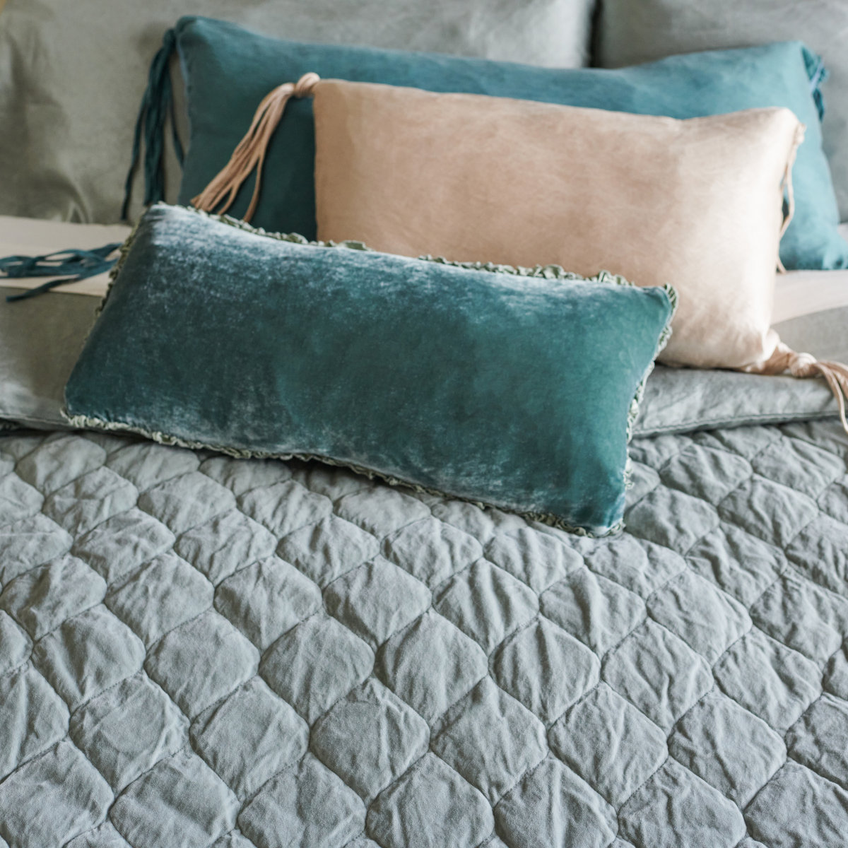 : Silk velvet and silk charmeuse throw pillows on a Harlow coverlet demonstrate how cotton velvet aborbs dye more subtly than vibrant silk blends - angled overhead view.