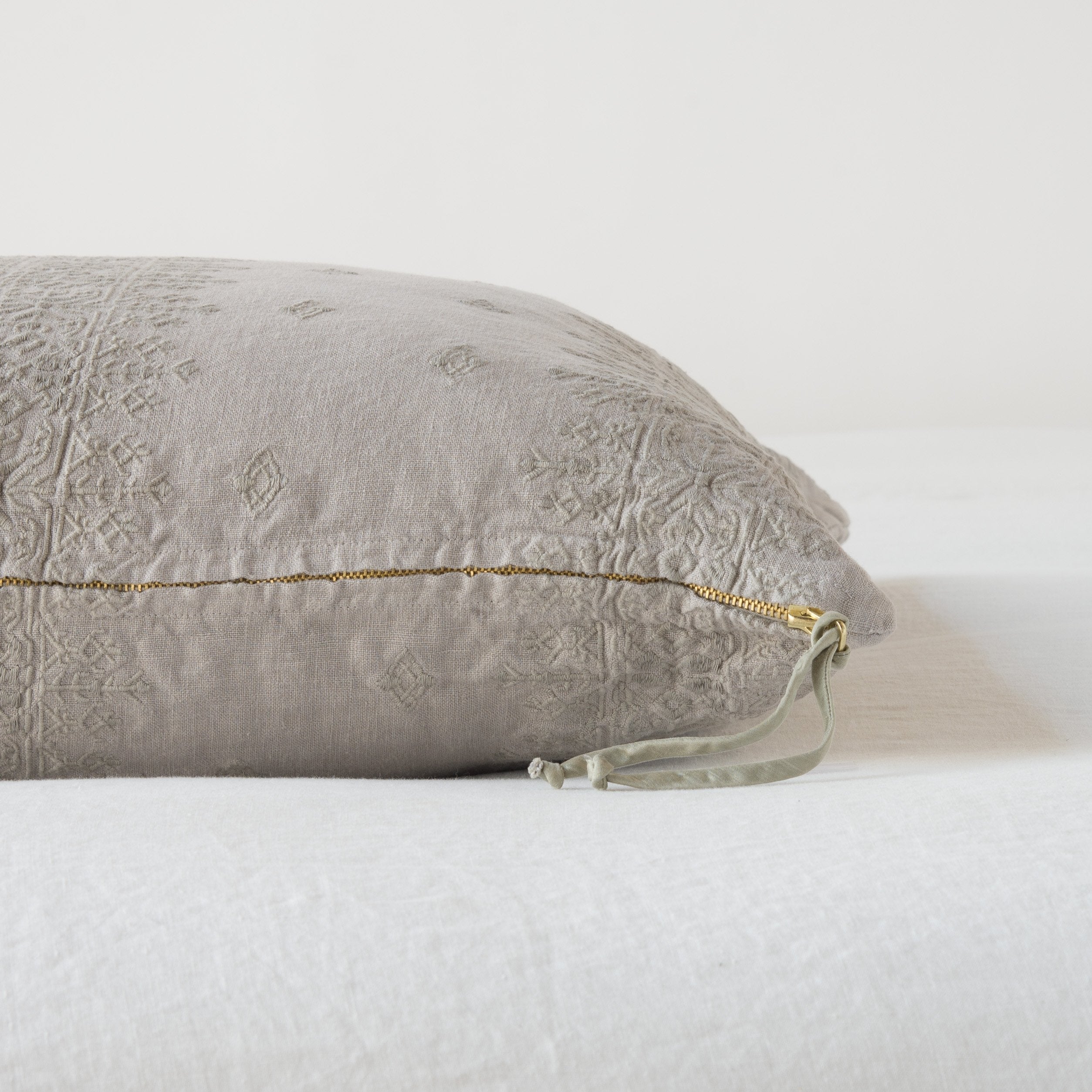 Fog: Close-up of brass zipper and charmeuse pull details on throw pillow - side view.