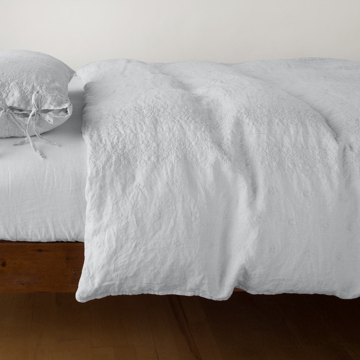 Sterling: lightly rumpled duvet cover on a monochromatic bed against a white background - side view.
