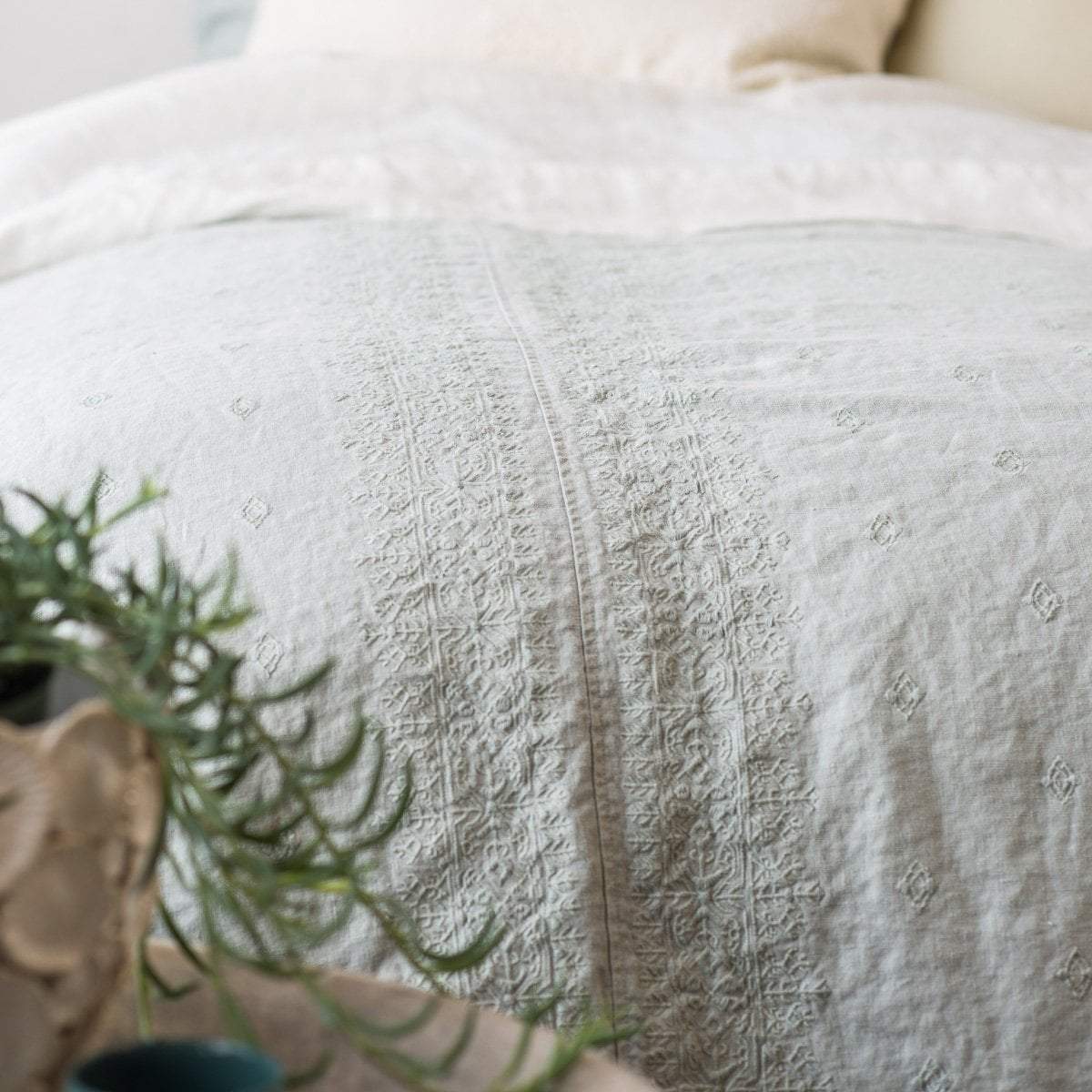 : Eucalyptus duvet cover on a bed with cream-toned sheeting, and greenery visible in the foreground - close-up end of bed view.
