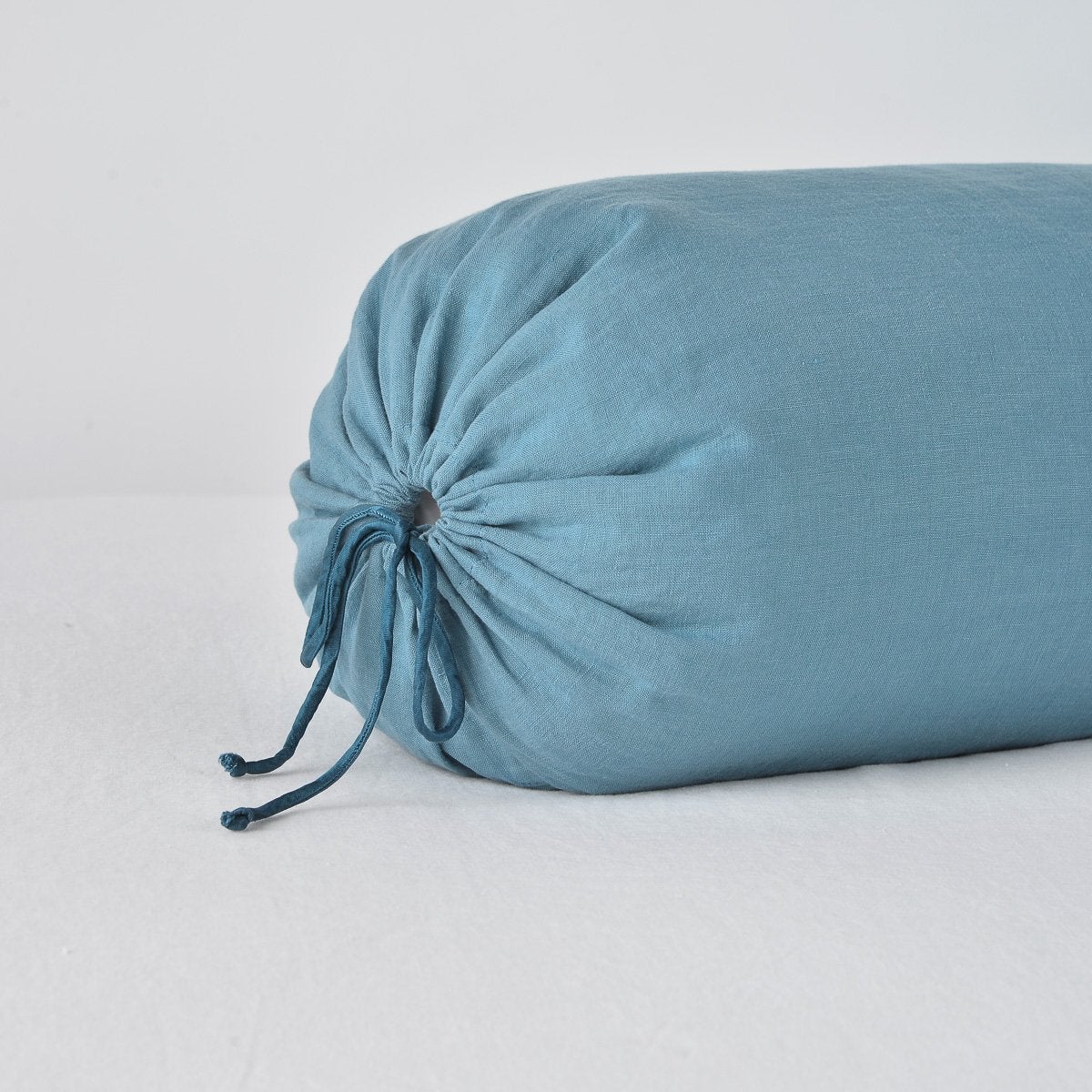 : Close-up of Linen bolster end detail in cenote, angled to show gathering and satin ties.